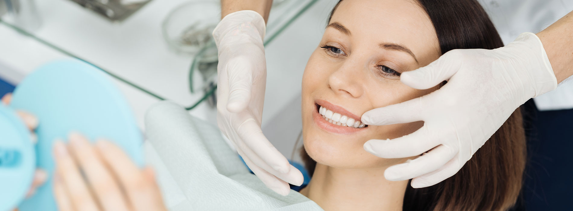 Woman sitting in dental chair with hands on her face, receiving dental treatment from a professional wearing gloves and a mask.